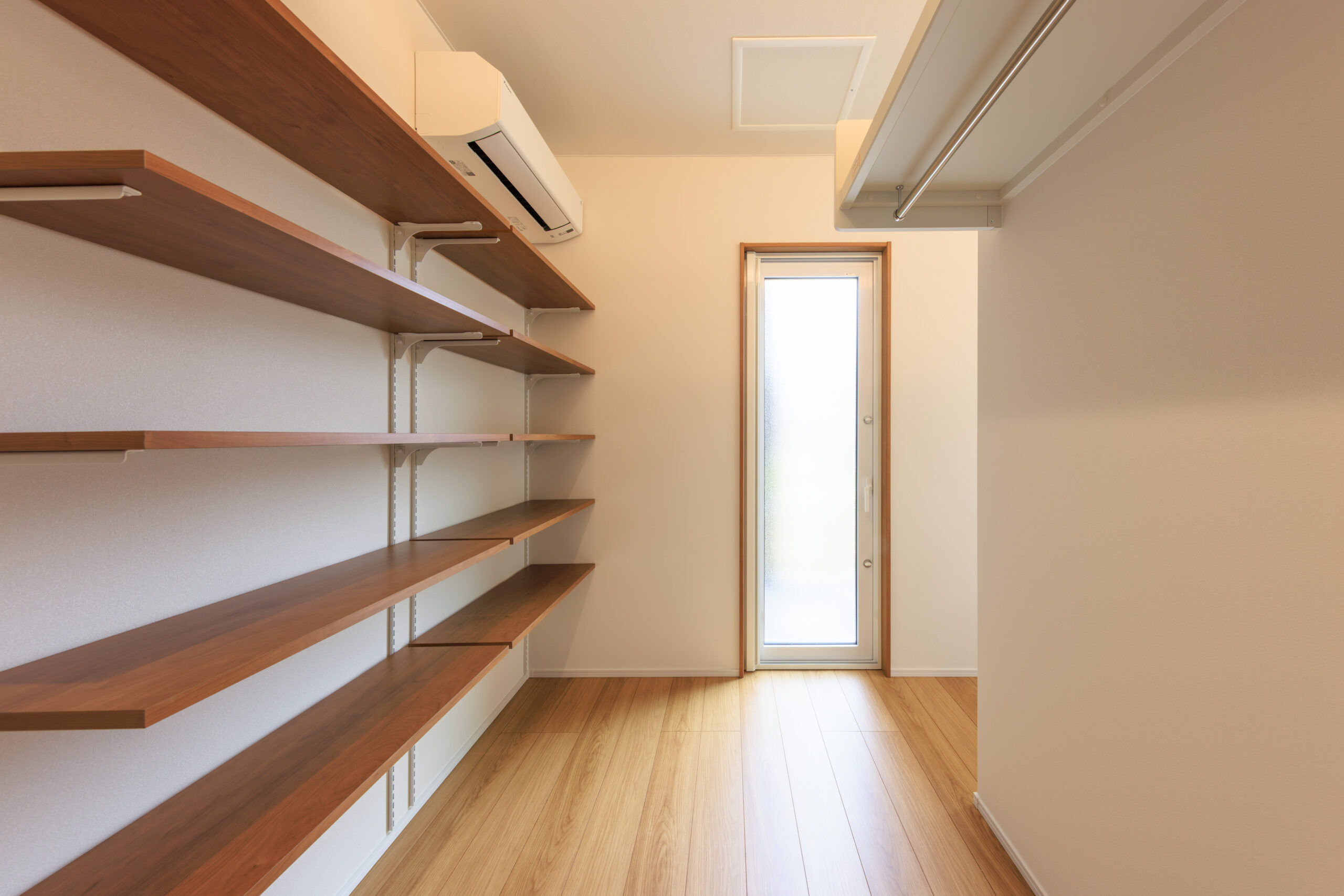 Narrow pantry with multiple wooden shelves along the left wall and a tall window at the far end.
