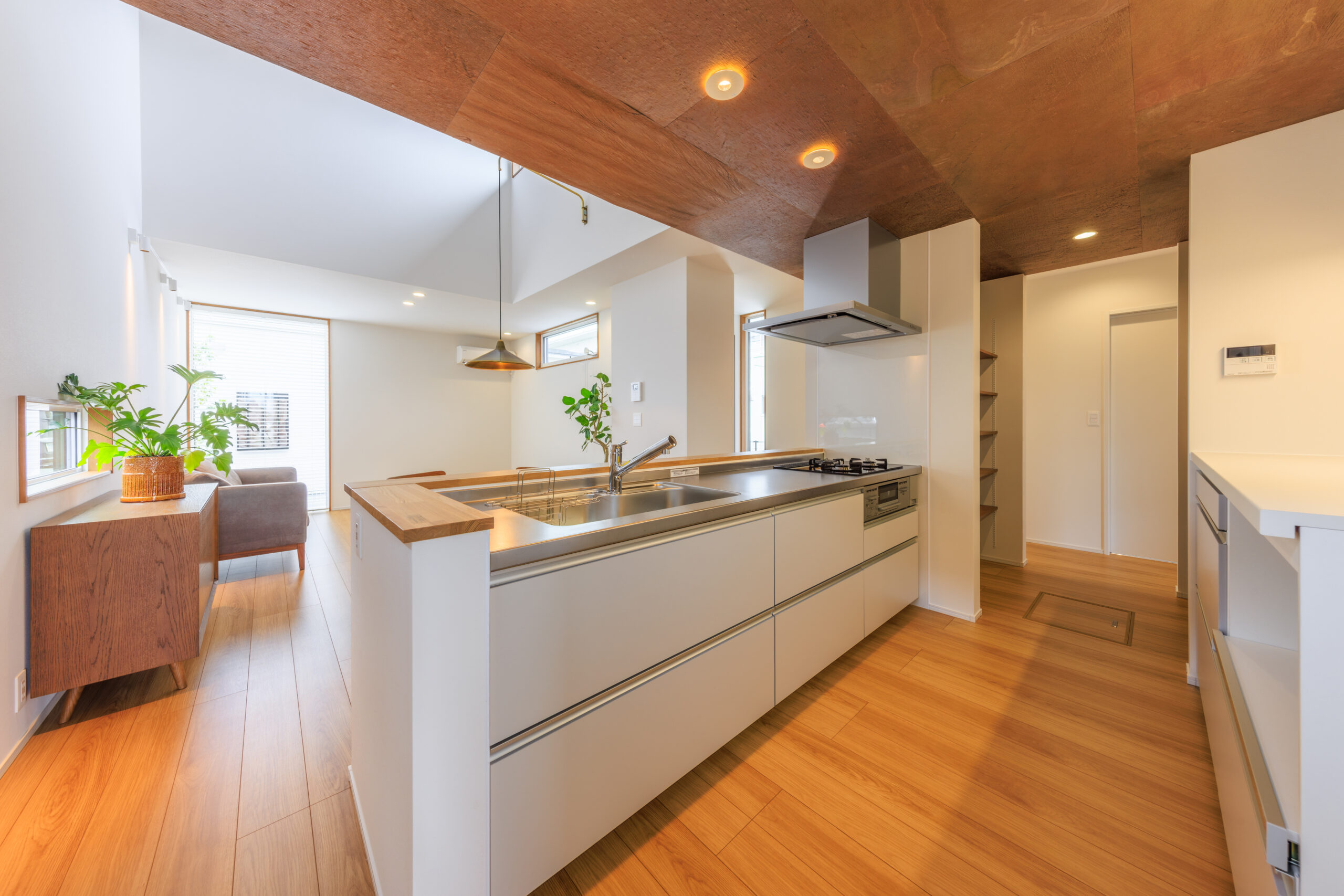 Open-concept kitchen and living area with a long white island, gas cooktop, stainless appliances, and a warm wooden sloped ceiling with recessed lights.
