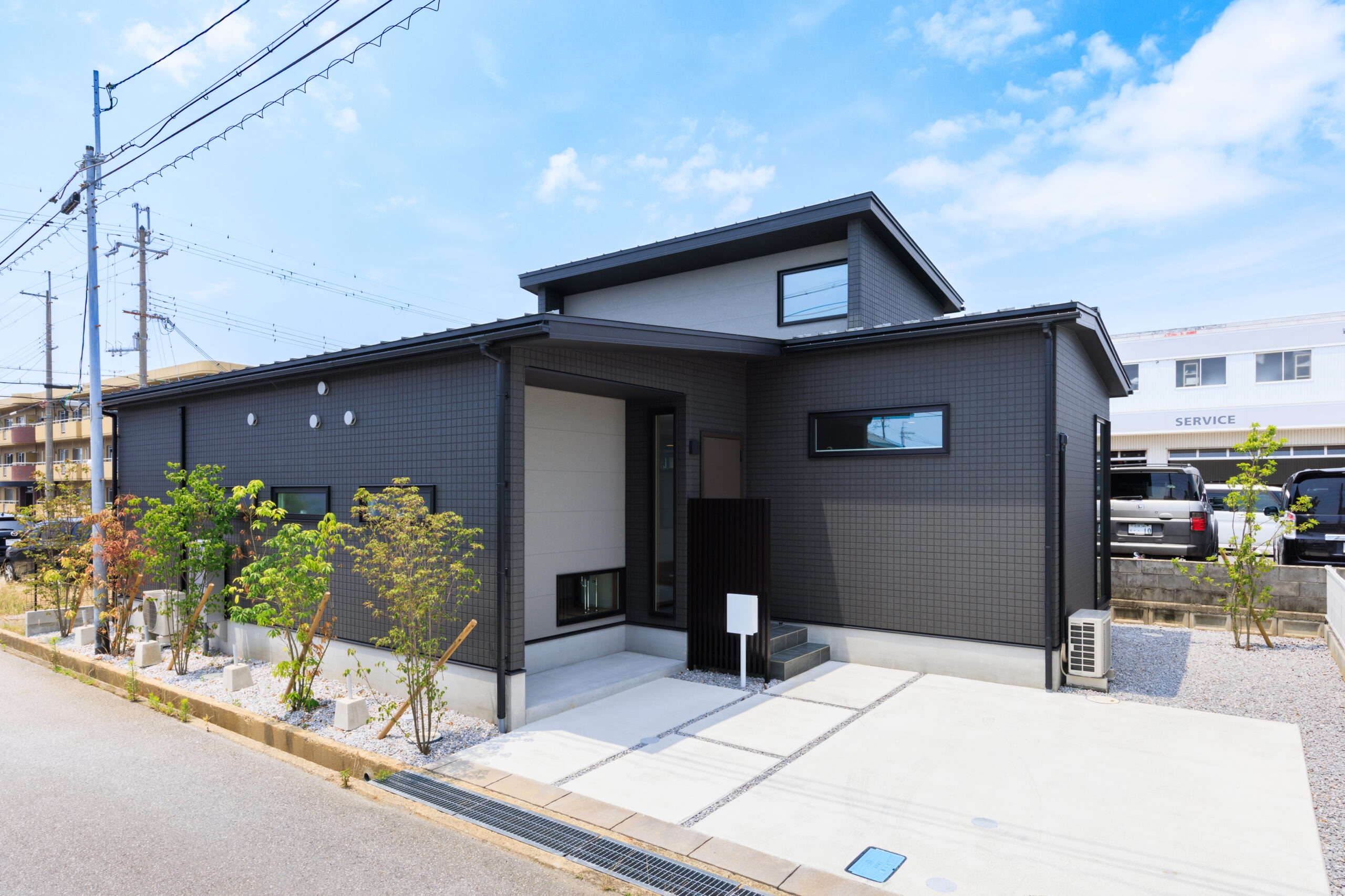 Modern dark-gray tiled house with a sloped roof, large windows, and a clean driveway against a blue sky.
